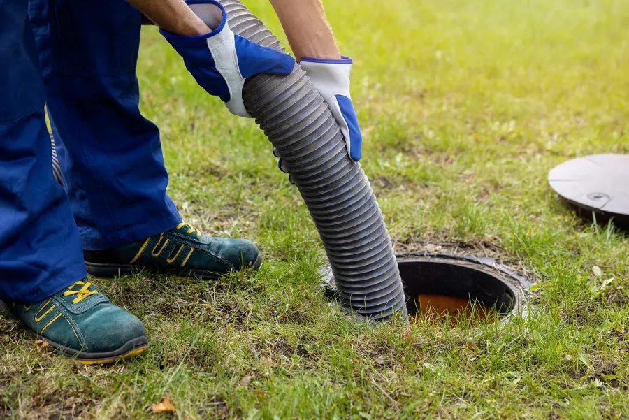 Technician guiding a vacuum hose into an open septic tank
